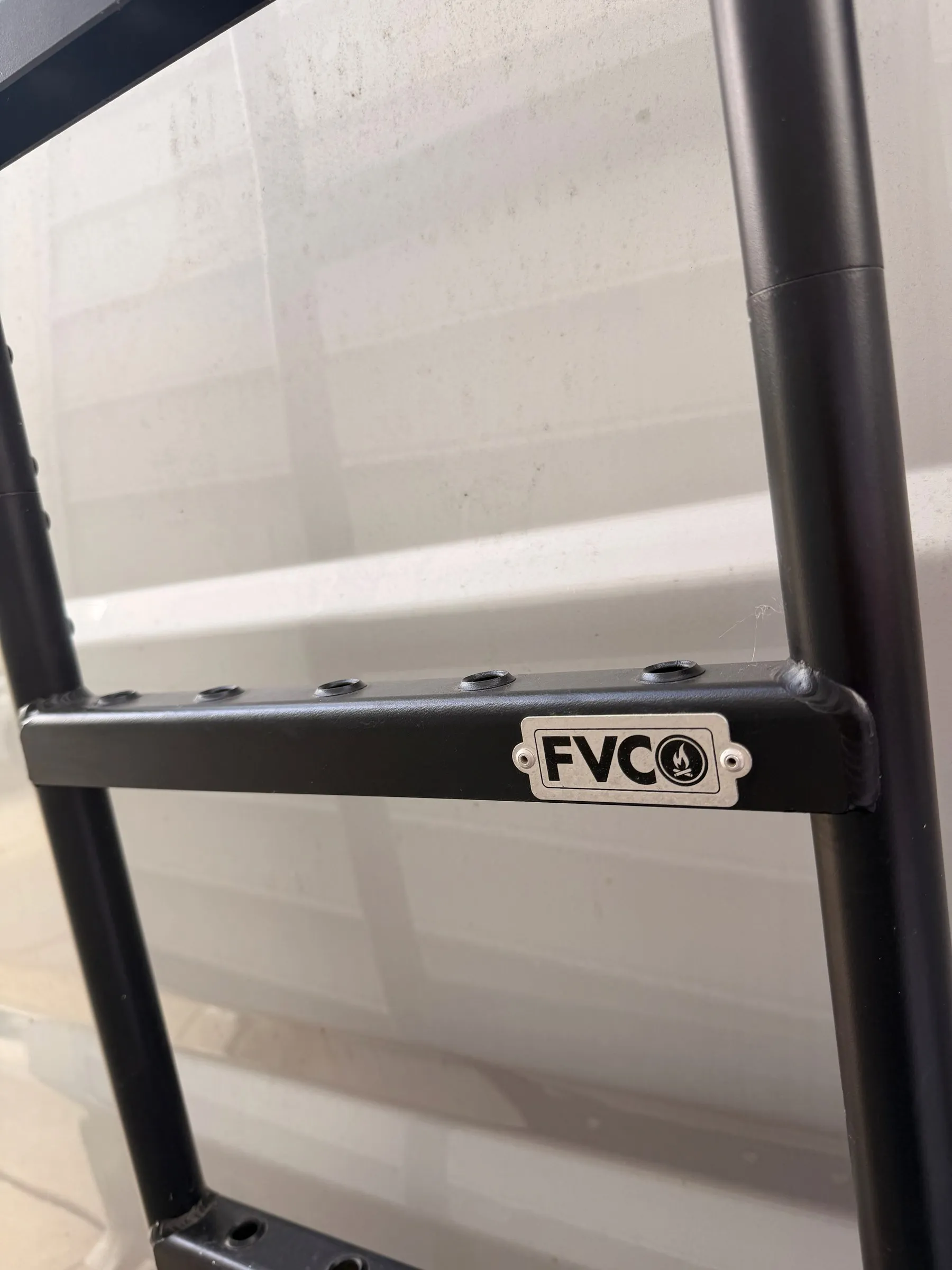 Close-up of the black FVCO rear ladder rung with brand plate against the silver van body