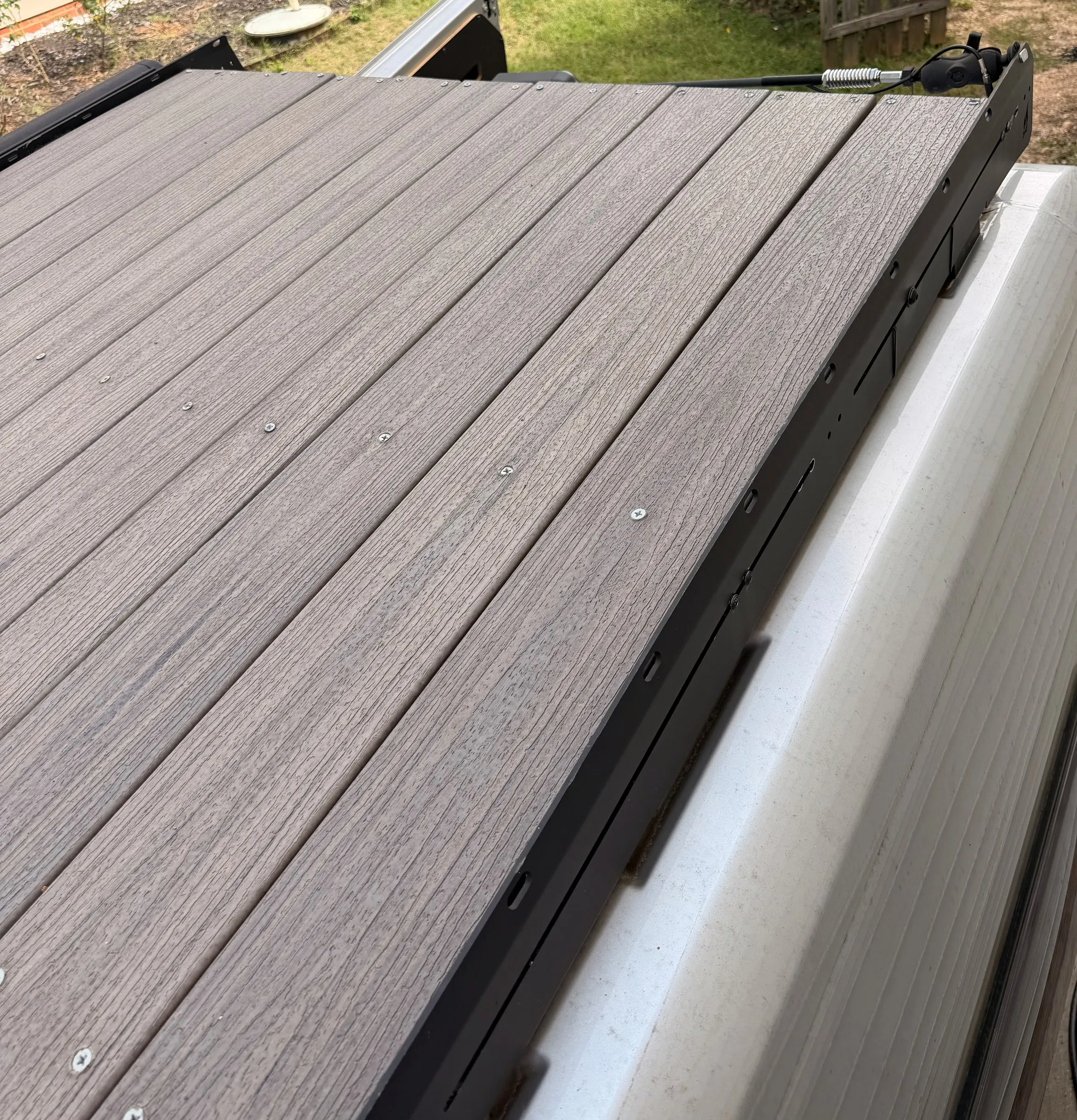 Gray wood-grain composite decking boards screwed to the black roof rack at the rear of the van