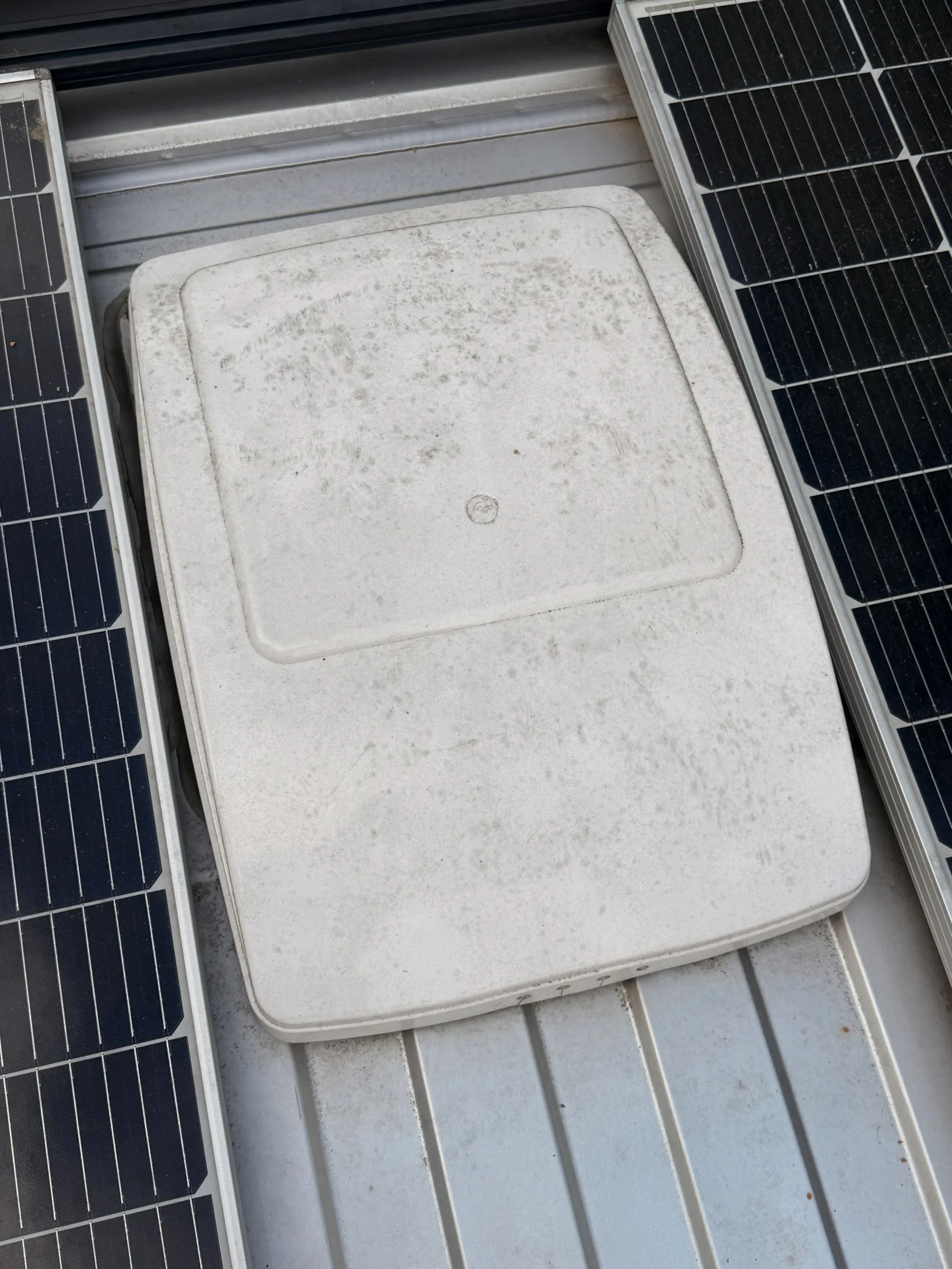 White roof vent fan cover installed between solar panels on the ribbed van roof